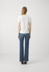 Camiseta blanca de manga corta combinada con jeans acampanados azules. La camiseta tiene un diseño sencillo; los jeans tienen bolsillos traseros y un borde rematado.