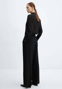 Zwarte blouse met lange mouwen, gecombineerd met hoge taille wijde broek, met een stijlvol ontwerp en een gladde textuur. Kenmerkende getailleerde pasvorm.