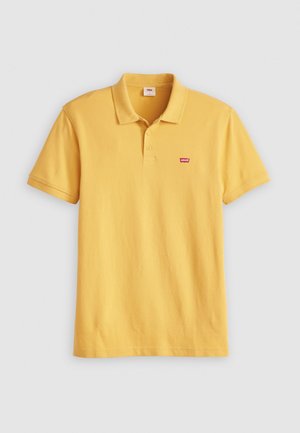 Camisa polo de algodón amarilla con una tapeta de tres botones, mangas cortas y un pequeño logo rojo de Levi's en el pecho. Textura suave.