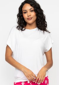 T-shirt bianco a maniche corte in tessuto liscio, con una vestibilità rilassata e scollo rotondo. Modello che indossa pantaloni da pigiama rosa con motivo.
