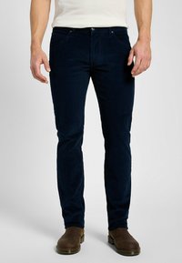 Pantaloni in velluto a coste blu navy con vestibilità slim, dotati di cinque tasche, chiusura con bottone in metallo e una sottile trama a coste verticali.