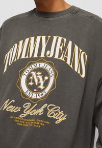 Felpa grigia con collo a giro, caratterizzata da una grande stampa grafica gialla e bianca, con un distintivo circolare che reca "NY" e "New York City".