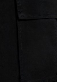 Czarna tkanina o gładkiej fakturze, z wyraźną kieszenią, prostym przeszyciem i subtelnym połyskiem. Gęsto tkany materiał.