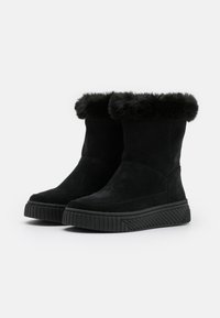 Une paire de bottes d'hiver noires mi-mollet avec des semelles en caoutchouc épaisses et un doublure en fourrure douce autour du bord supérieur, légèrement inclinées vers la gauche.