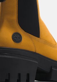 Chelsea-Stiefel aus senfgelbem Wildleder mit schwarzen elastischen Seiteneinsätzen. Verfügt über eine strukturierte Gummisohle und ein rundes Logo-Patch.