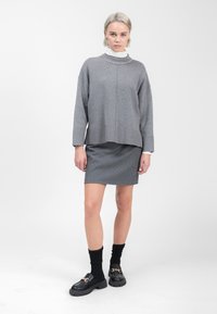 Grijze gebreide trui met een textuur in de halslijn, gecombineerd met een grijze rok met kleine witte stippen. Zwarte loafers met dikke zolen en sokken.