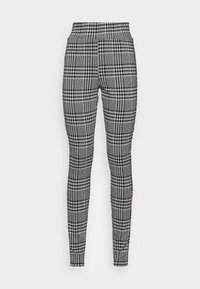 Leggings à carreaux noir et blanc avec taille haute. Le tissu présente un motif texturé avec des carreaux contrastants et un design pied-de-poule.