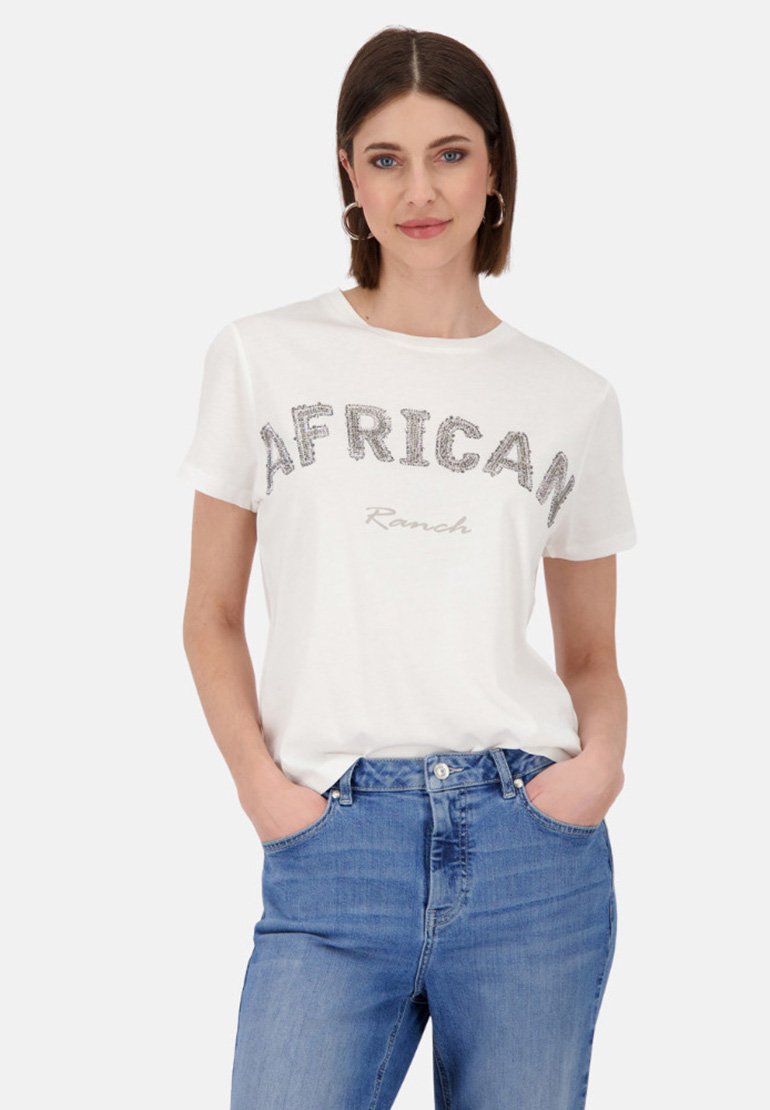 Weißes Baumwoll-T-Shirt mit dem Wort "AFRICAN" in silberglänzenden Buchstaben und "Ranch" darunter in Grau, kombiniert mit blauen Jeans.