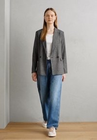Blazer cinza em padrão herringbone com dois botões, combinado com jeans de perna larga azul claro e ténis brancos. Tecido suave e corte ajustado.