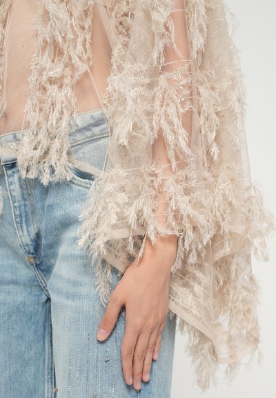 Durchsichtiger beiger Kimono mit strukturierten federähnlichen Akzenten, über hellblauer Denim mit metallischen Verzierungen und lockerem Schnitt.