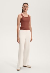 Copper ribbed tank top paired with cream wide-leg trousers, featuring a smooth texture and side pockets. Footwear includes white sneakers.