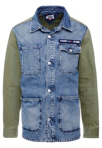 Denimtakki vihreillä kangas hihoilla, napit kiinnityksellä, kaksi etutaskua ja brändilogo rinnassa, joka esittelee erilaisten tekstuurien sekoitusta.