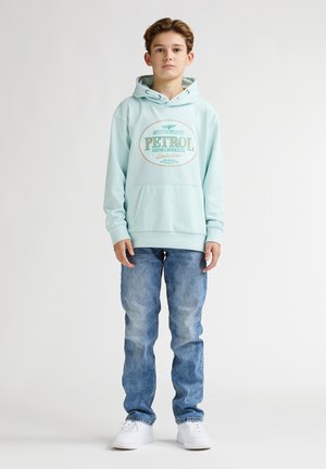 Sweat à capuche turquoise clair avec un motif graphique sur le devant, doté d'une poche kangourou, associé à un jean bleu délavé et des baskets blanches. Design simple, coupe décontractée.