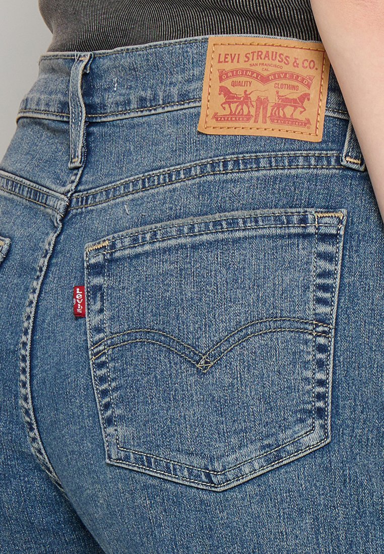 Jeans de mezclilla con un lavado azul claro, que presentan una etiqueta de cuero con logo, costuras icónicas en el bolsillo trasero y una pequeña etiqueta roja en el lateral.