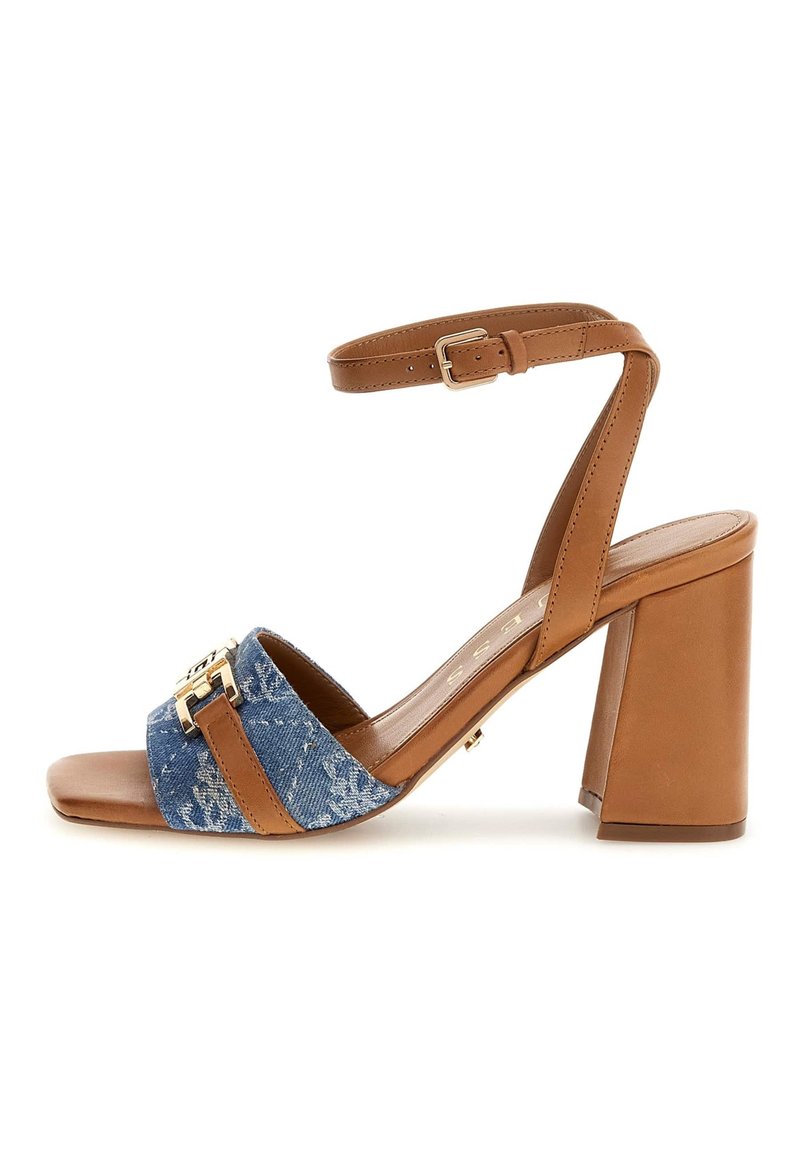 Tan block heel sandal featuring a denim fabric upper, two wide straps, a gold buckle accent, and an adjustable ankle strap.