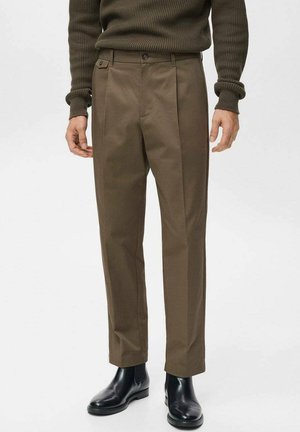 Brown tailored trousers with a smooth texture, featuring front pleats and a square button detail. Paired with black ankle boots.