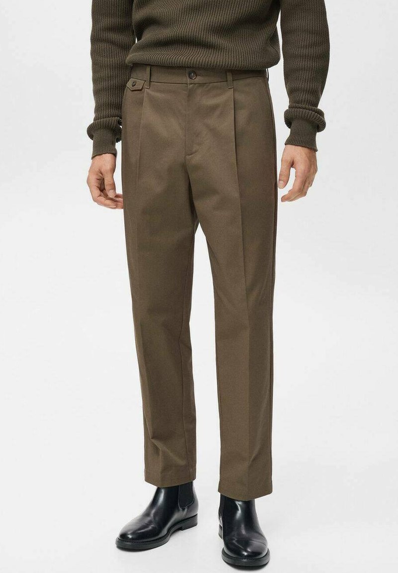 Brown tailored trousers with a smooth texture, featuring front pleats and a square button detail. Paired with black ankle boots.