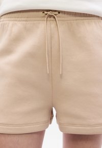 Shorts en mélange de coton beige avec taille élastique, cordon de serrage et ourlet cousu. Texture lisse et design minimaliste.