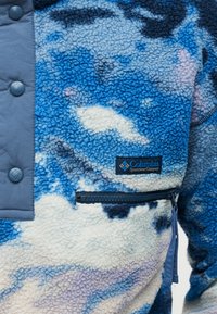 Κοντινό πλάνο μπλε, λευκού και μοβ φλις μπουφάν με ετι κέτα Columbia Sportswear, τσέπη με φερμουάρ και κουμπιά snap στο μπροστινό πάνελ.