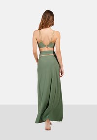 Conjunto verde de dos piezas que incluye una blusa ajustada con detalles dorados y una falda maxi fluida. Tejido suave con una textura lisa y tirantes ajustables.