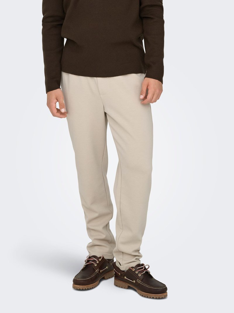 Beige sweatpants with a tapered leg design, made from a soft fabric, paired with dark brown shoes featuring laces and a textured sole.