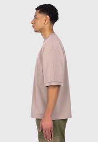 Kurze Ärmel, T-Shirt mit Rundhalsausschnitt aus leichtem Taupe-Baumwollstoff. Verfügt über einen lockeren Sitz und gerippte Bündchen. Kombiniert mit olivgrünen Cargo-Hosen.
