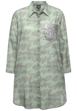 Camisa de botones verde claro de tela suave, con un patrón abstracto gris y un bolsillo en el pecho adornado con lentejuelas. Mangas de ¾ de longitud.