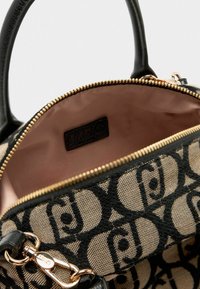 Borsa da designer aperta con motivo nero e beige, zip dorata, manici in pelle nera e interno in tessuto rosa con etichetta del marchio.
