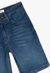 Pantalones cortos de mezclilla con una textura suave, presentan un lavado azul oscuro, desgaste visible y costuras en dorado contrastante.