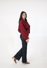 Bordowa krótka kurtka z bufkami na rękawach i dwoma przednimi kieszeniami, zestawiona z ciemnymi dżinsami typu flare i beżowymi botkami na obcasie.