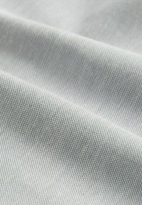 Tejido de color gris claro con una trama fina y texturizada, que presenta pliegues suaves y caídos, así como un sutil brillo.