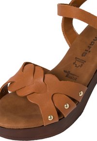 Sandale compensée en cuir marron avec des brides en forme de papillon, détails en rivets dorés et semelle intérieure rembourrée, conçue pour un style décontracté.