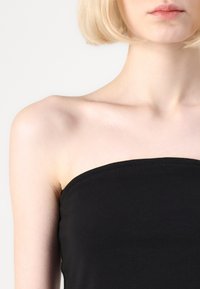 Svart strapless topp i mjukt tyg, med en slät textur och en figurnära design som framhäver dekolletaget och axlarna.