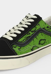 Χαμηλό sneaker με λευκά κορδόνια, μαύρη μύτη, ύφασμα με πράσινο σχέδιο φιδιού, μαύρη πλαϊνή ρίγα και λευκή λαστιχένια σόλα.