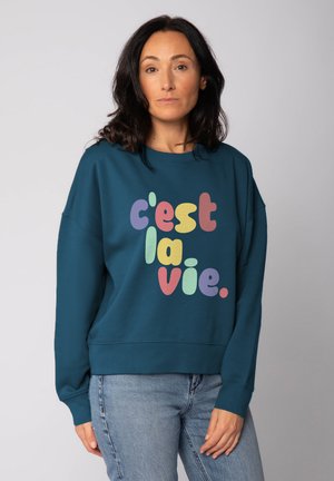 Teal oversized sweatshirt met kleurrijke, speelse tekst "c'est la vie" in verschillende pastelkleuren. Heeft lange mouwen en een ronde hals.