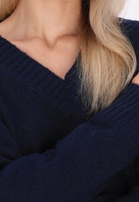 Pull bleu marine avec un col en V, des poignets côtelés et un tissu doux et texturé. Vue en gros plan du col et du détail du bras.