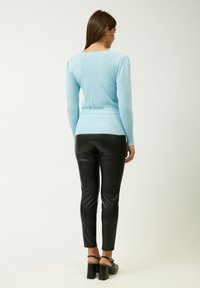 Top azzurro chiaro a maniche lunghe con scollatura quadrata, texture a coste, abbinato a pantaloni in pelle nera a vita alta e sandali con tacco.