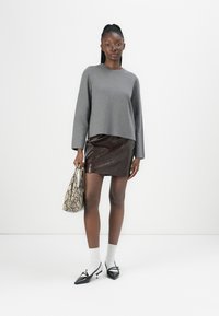 Grå langermet genser, brun blanke faux-lær mini skjørt, trykt slangeremønster håndveske, hvite sokker, svarte spisse sko.