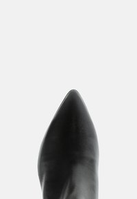 Pantof cu vârful ascuțit din piele neagră, pe un fundal alb simplu, văzut de sus, concentrându-se pe vârful din față.