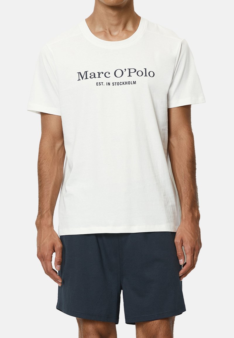 Weißes Baumwoll-T-Shirt mit dem Aufdruck "Marc O'Polo EST. IN STOCKHOLM" in Marineblau. Kombiniert mit dunkelblauen Shorts. Schlichtes Design, Rundhalsausschnitt.