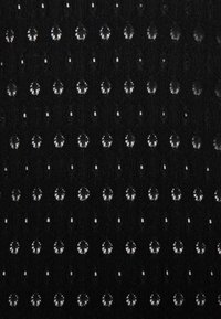 Svart tyg med upprepade cirkulära utskärningar som skapar ett mönster av överlappande ovala former, blandat med små fyrkantiga öppningar.