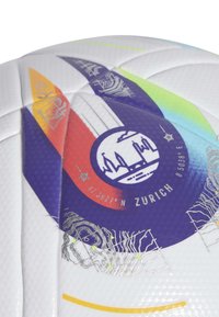 Pallone da calcio bianco con superficie testurizzata. Presenta motivi geometrici colorati in rosso, blu, giallo e verde. Il logo centrale include le coordinate.