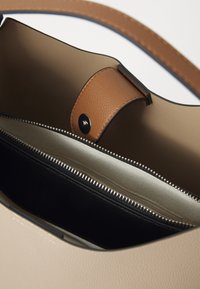 Borsa beige con tracolla in pelle marrone. L'interno presenta un compartimento con zip nera e una fodera di colore chiaro, che mette in evidenza texture morbide.