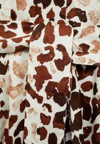 Tissu marron et blanc présentant un motif léopard avec des taches irrégulières et une texture douce, drapé avec une section nouée.