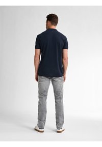 Navy sininen polo-paita lyhyillä hihoilla, istuva malli, yhdistetty vaaleanharmaisiin farkkuihin ja valkoisiin lenkkikenkiin; yksinkertainen takanäkymä.