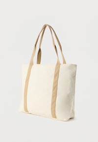 Καμβά τσάντα ώμου σε κρεμ χρώμα με αντίθετες μπεζ λουριά. Διαθέτει ορθογώνιο σχήμα και λεία υφή, ιδανική για καθημερινή χρήση.