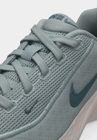 Ανοιχτό γκρι αθλητικό παπούτσι Nike για τρέξιμο με άνω μέρος από δίχτυ, γκρι κορδόνια και σκοτεινό γκρι λογότυπο Swoosh στο πλάι, σε κοντινή λήψη του μπροστινού και πλαϊνού μέρους.