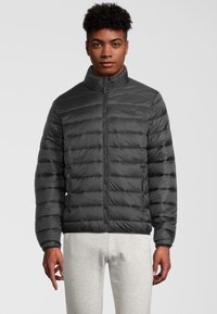 Svart puffjacka med kviltat mönster, hög krage, zip-up framknäppning och sidofickor. Slät textur med subtila logodetaljer.