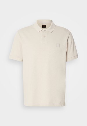 Short-sleeve polo shirt in light beige, made of soft fabric, featuring a buttoned placket and a small logo patch on the chest.