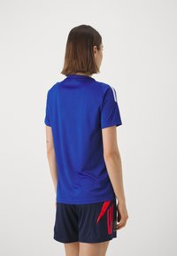 Blauwe sportieve polo met korte mouwen en een kraag, met witte accenten op de schouders. Draag het met marineblauwe shorts.